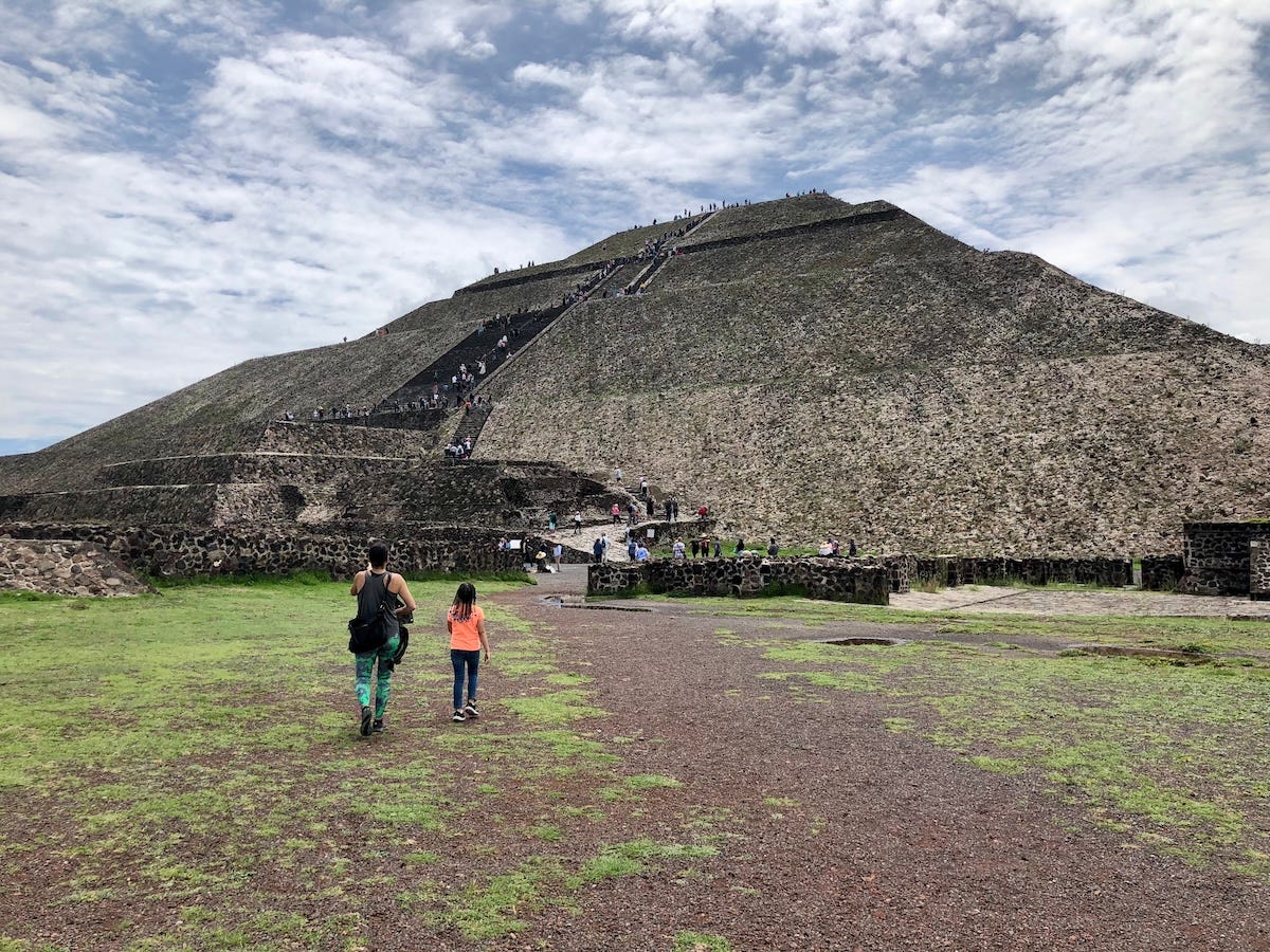 Visitors approach and climb the Pyramid of the Moon at Teotihuacan, a massive stepped stone structure set against a partly cloudy sky. My wife and daughter approaching the Pyramid of the Moon at Teotihuacan Visitors approach and climb the Pyramid of the Moon at Teotihuacan, a massive stepped stone structure set against a partly cloudy sky. My wife and daughter approaching the Pyramid of the Moon at Teotihuacan
