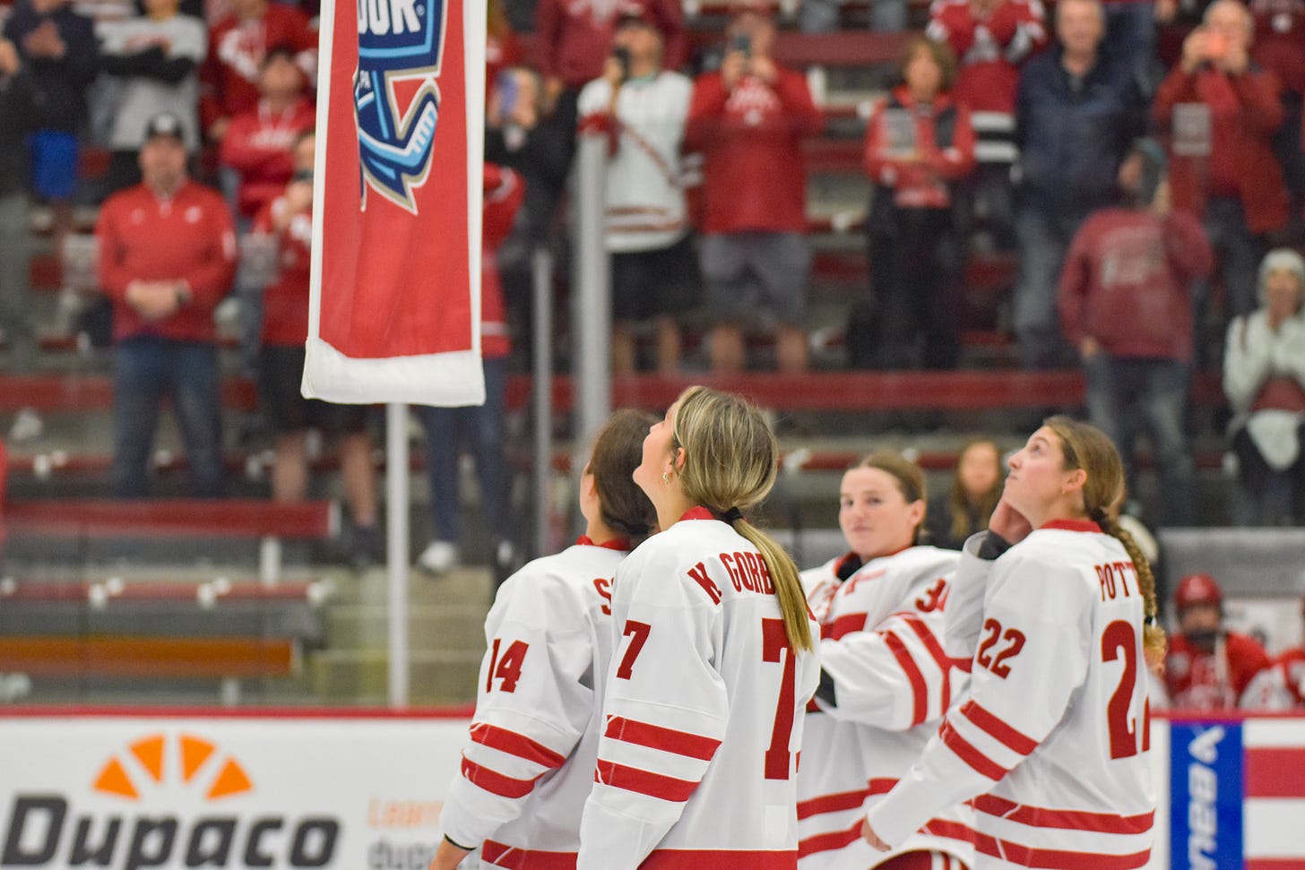 with the 2026 national championship banner just above their heads, Wisconsin's captains title their head upward to watch it raised