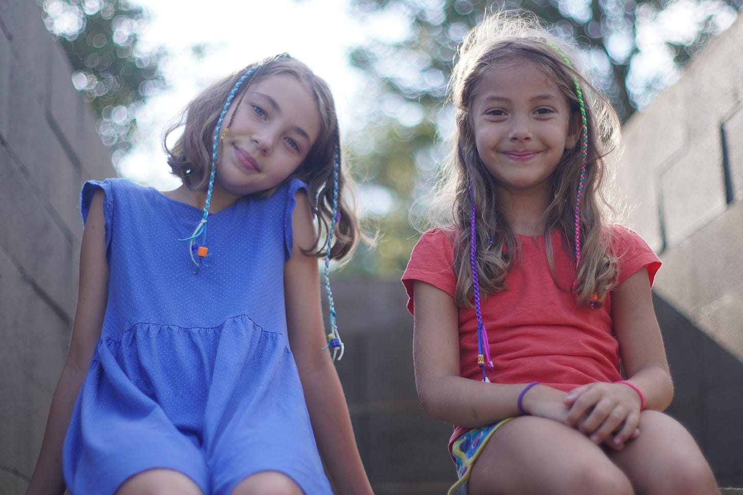 Two girls sit on a stone stairwell in the sun