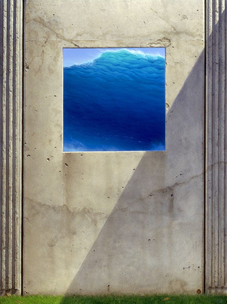 A smooth stone facade, reminiscent of a gravestone, occupies the entire foreground of the painting. A square window set into the top center offers a vision of a vibrant blue wave cresting at enormous height and about to crash down. A diagonal shadow cuts across the face of the stone. Three embossed ridges border each side of the stone. Green grass can barely be seen at its base. A smooth stone facade, reminiscent of a gravestone, occupies the entire foreground of the painting. A square window set into the top center offers a vision of a vibrant blue wave cresting at enormous height and about to crash down. A diagonal shadow cuts across the face of the stone. Three embossed ridges border each side of the stone. Green grass can barely be seen at its base.