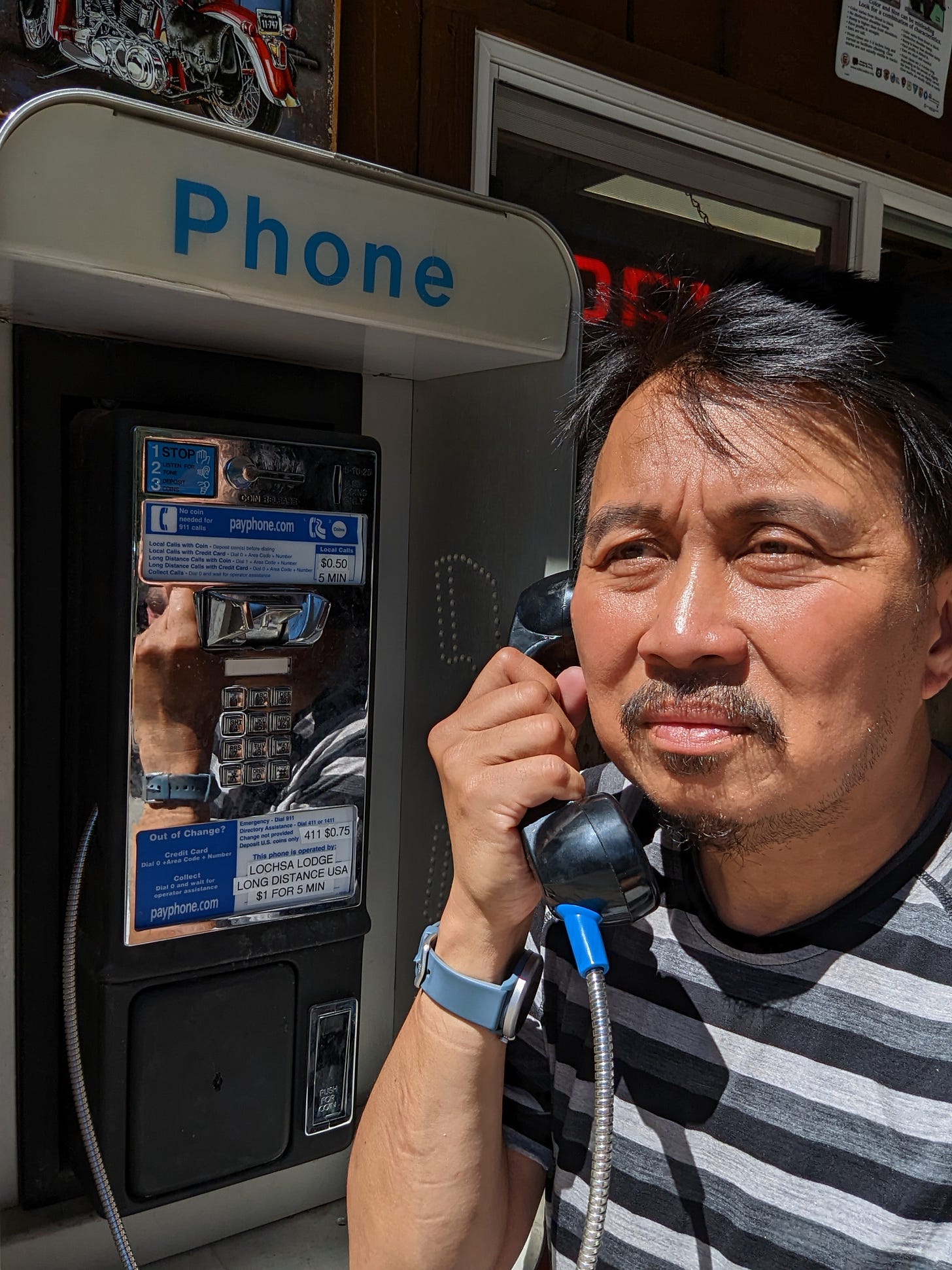 Man (me) pretends to be making a phone call at an old phone booth.