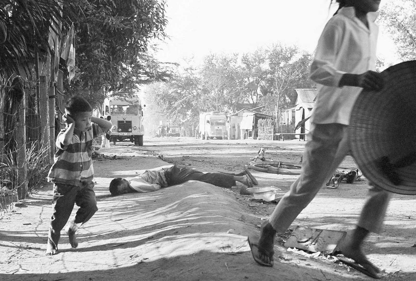 January 31, 1968, Da Nang: A poignant scene of a young Vietnamese boy fleeing gunfire, shielding his ears, as a dead civilian lies nearby on the street. January 31, 1968, Da Nang: A poignant scene of a young Vietnamese boy fleeing gunfire, shielding his ears, as a dead civilian lies nearby on the street.