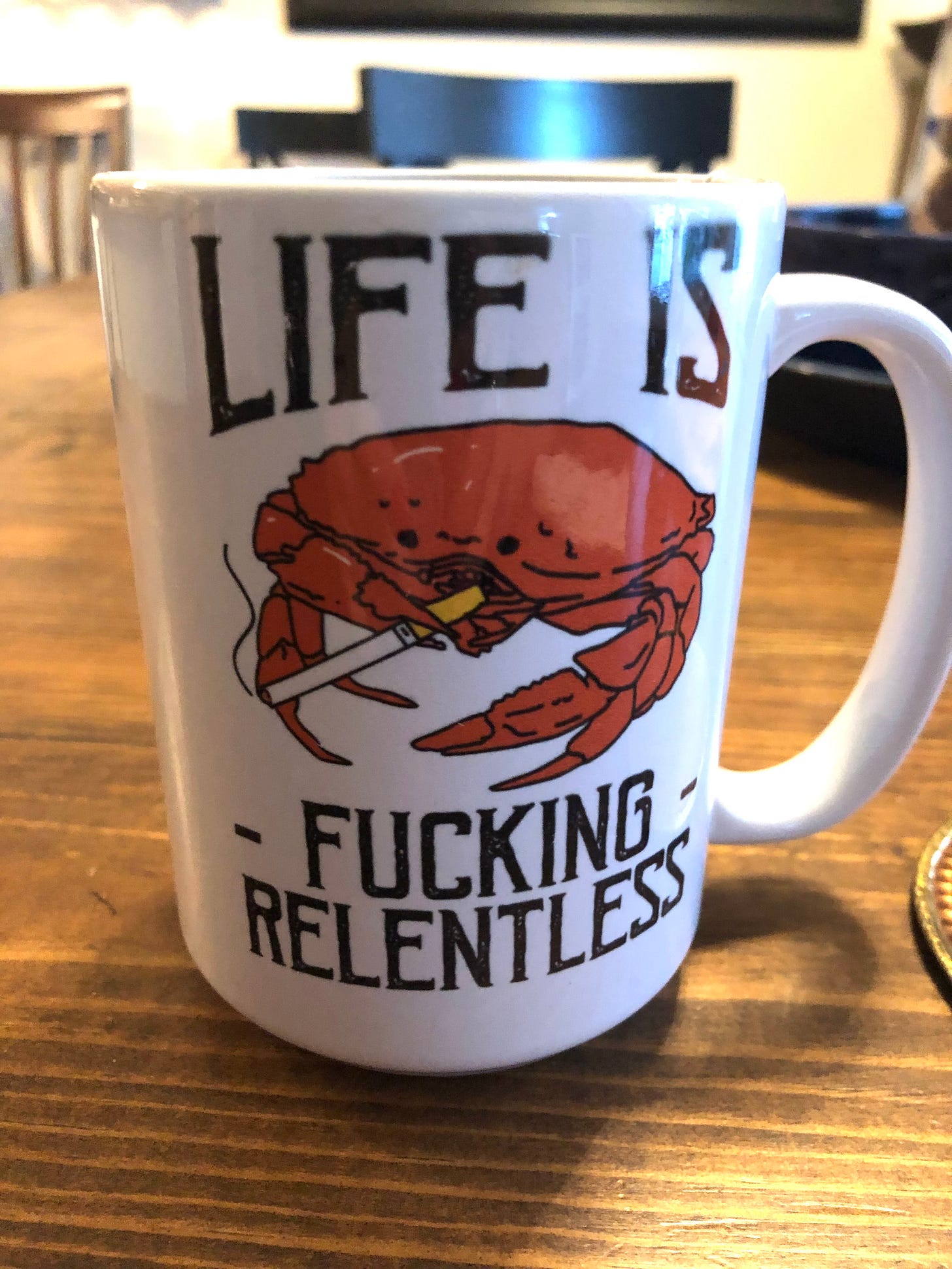 A coffee mug with teh image of a red crab smoking a cigarette with the text “Life is fucking relentless.” A coffee mug with teh image of a red crab smoking a cigarette with the text “Life is fucking relentless.”