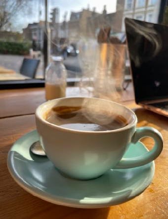 A turquoise cup of coffee on a cafe table looking out of a window, steam rises from it
