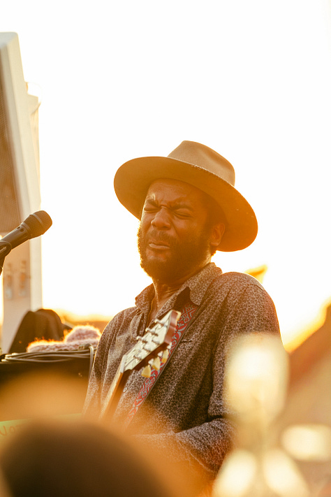 A collage of five photos of Gary Clark Jr. performing outdoors. The images are a mix of color and black and white, featuring close-ups of his face as he sings and wider shots of him playing the guitar, all while wearing his signature hat.