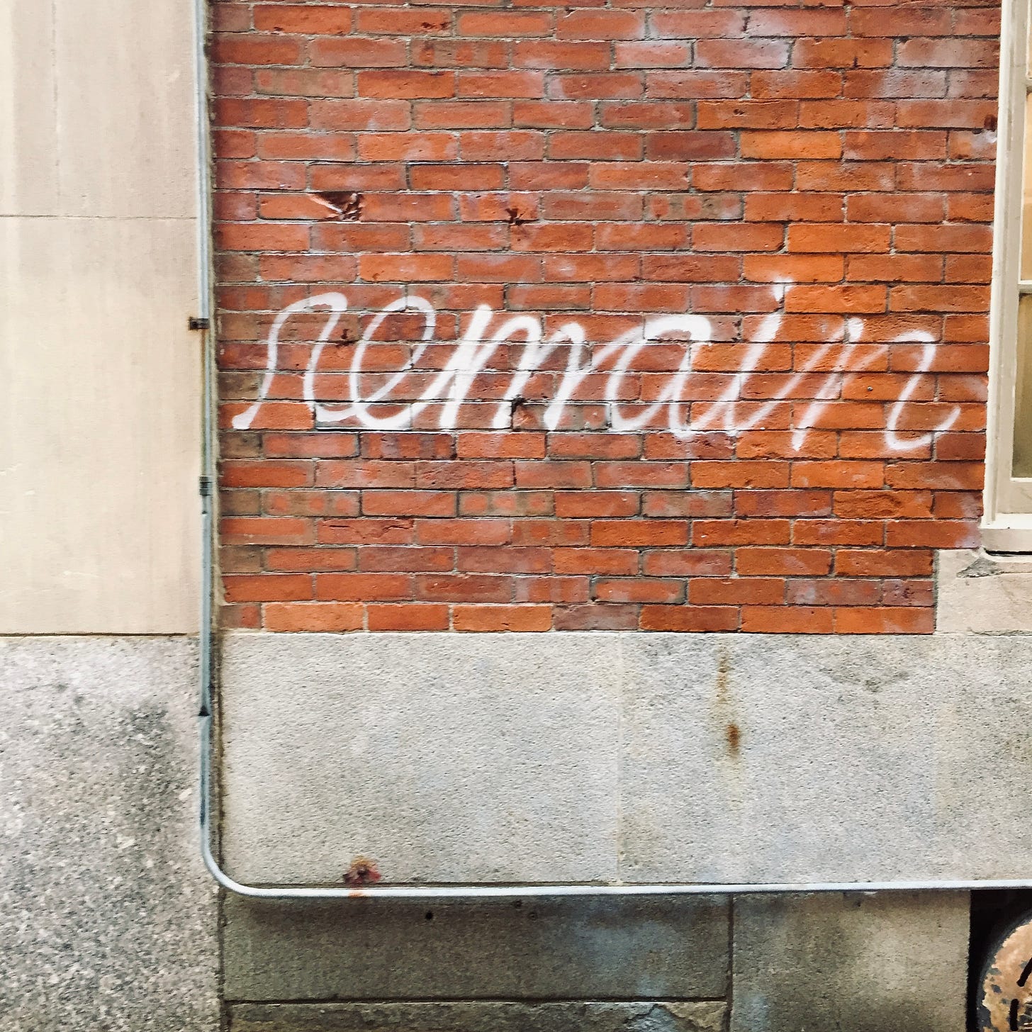 The word "remain" spray-painted in cursive on a red brick wall