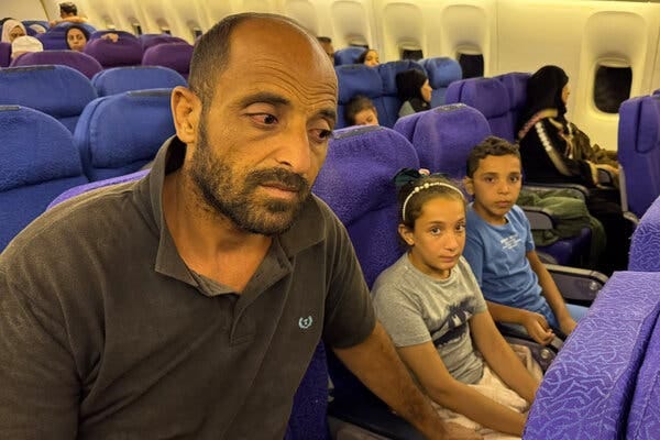 A pensive-looking man sits next to a young girl and boy on a plane.