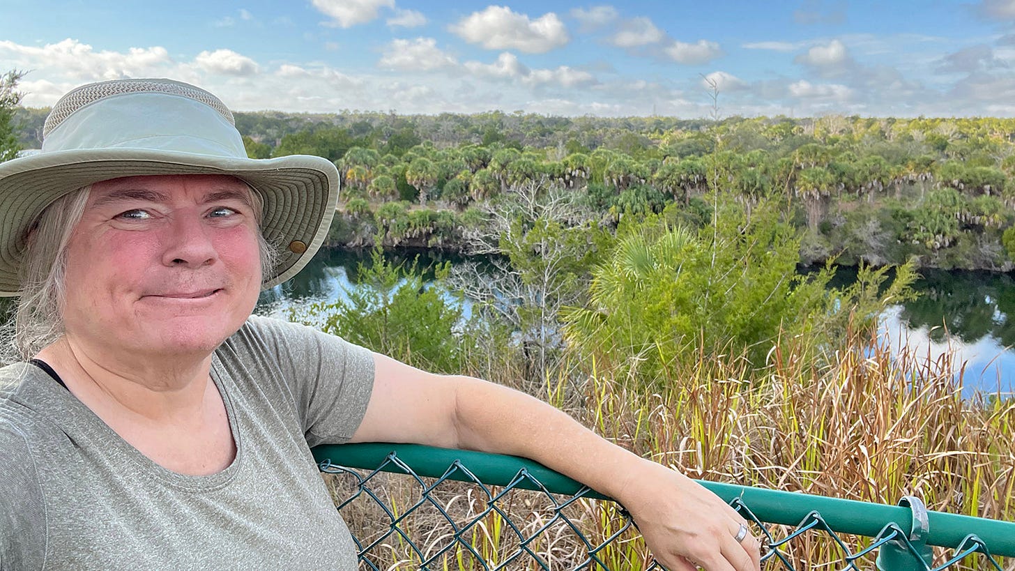 Sandra in front of a dropoff into a water-filled quarry with a long view to horizon