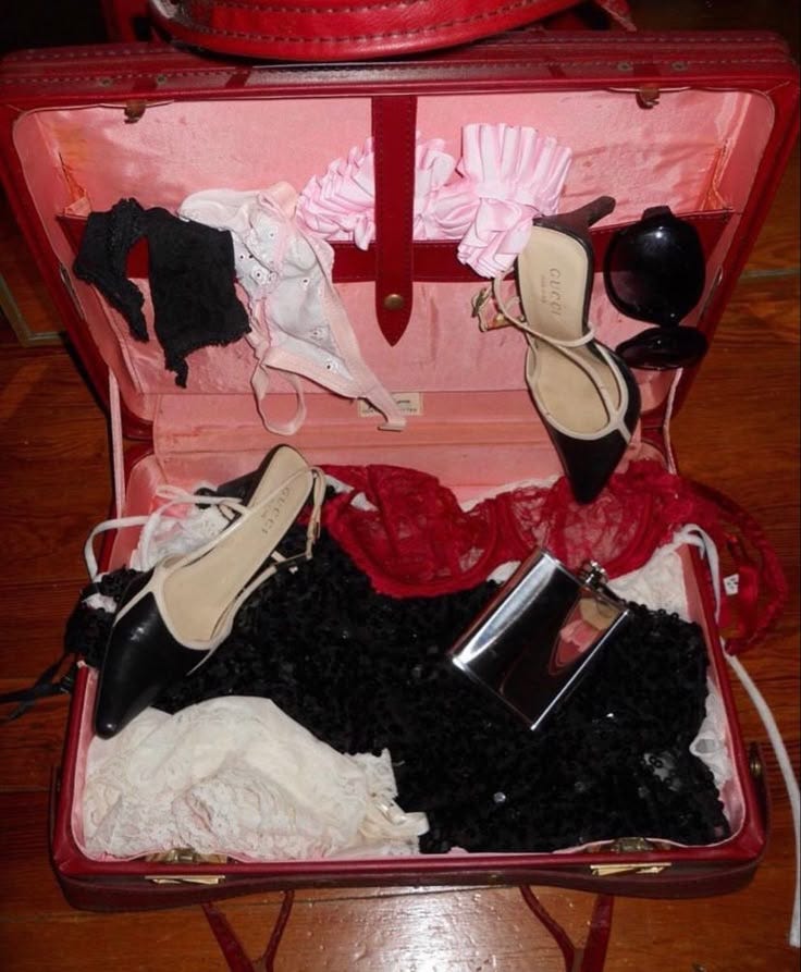 This may contain: an open suitcase filled with shoes and other items on top of a wooden floor next to a red purse