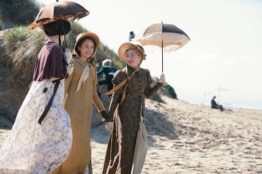 Three Regency women walking on the beach with parasols. 