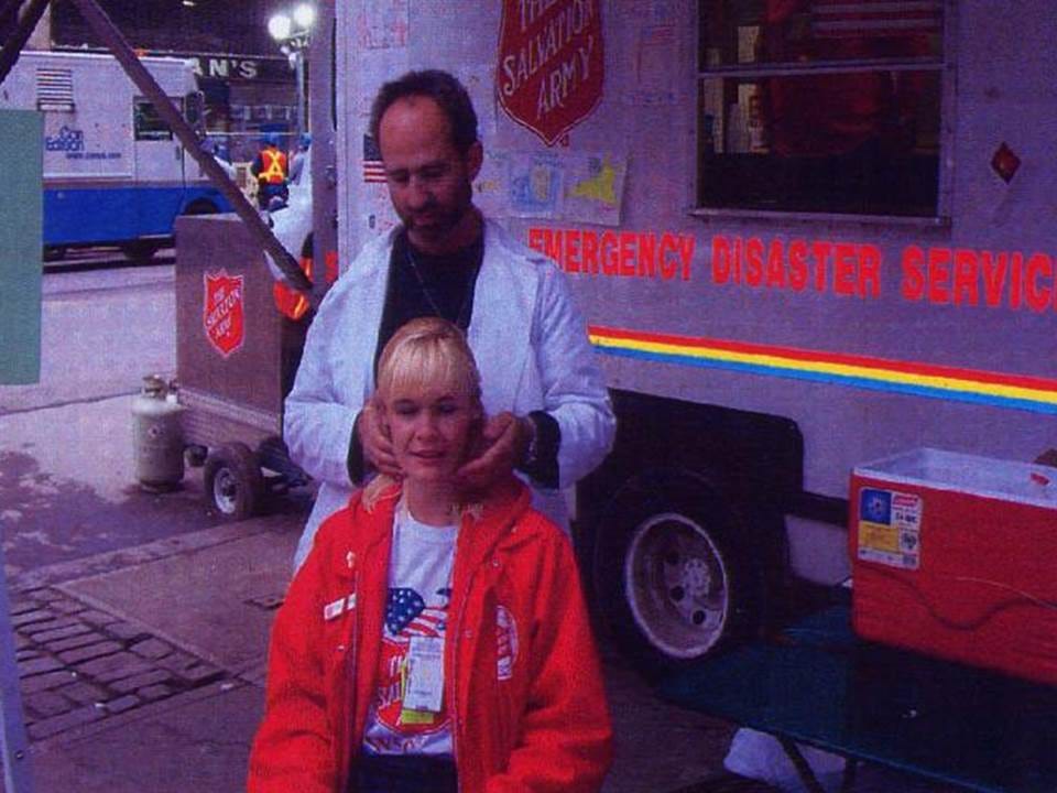 Chiropractor in a white coat adjusts a seated woman's neck beside a Salvation Army disaster services truck