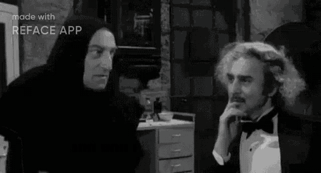 a man in a tuxedo is talking to another man in a black and white photo .