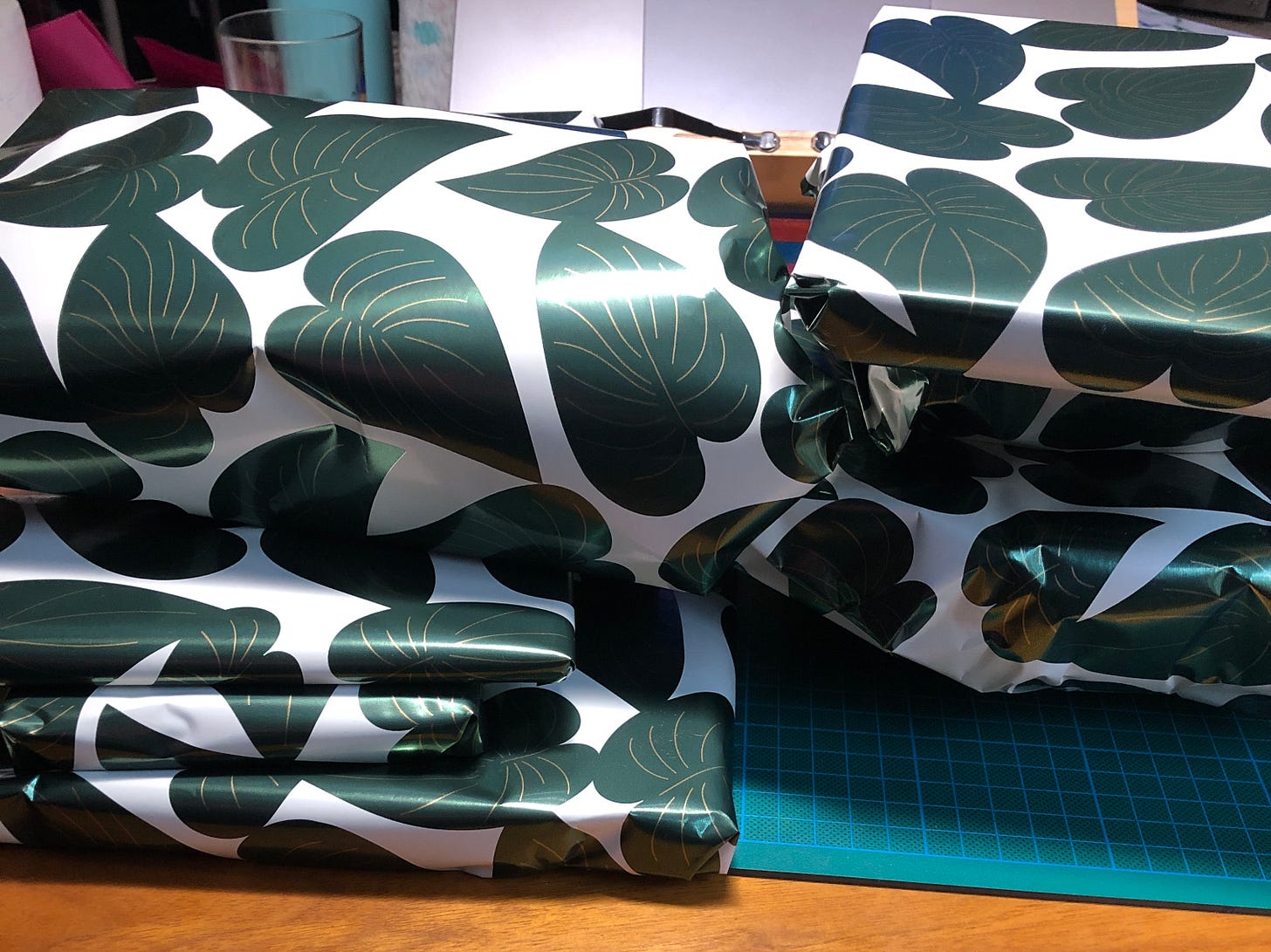 Une pile de cadeaux posés sur mon tapis de découpe. Le papier cadeau est à motif de feuilles de plantes type pothos.