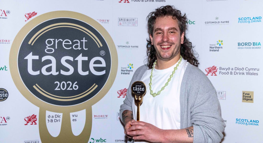 A man - Jake Goldstein- holding a golden fork next to a Great Taste logo A man - Jake Goldstein- holding a golden fork next to a Great Taste logo