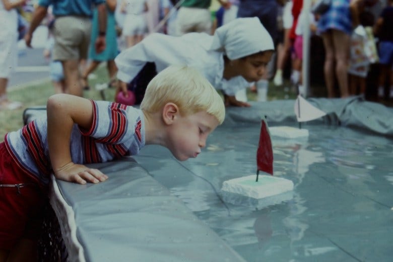 Children blow air out of their mouths to push styrofoam boats in water during the 1985 Artscape. Image courtesy of the Baltimore Office of Promotion & Arts. Children blow air out of their mouths to push styrofoam boats in water during the 1985 Artscape. Image courtesy of the Baltimore Office of Promotion & Arts.