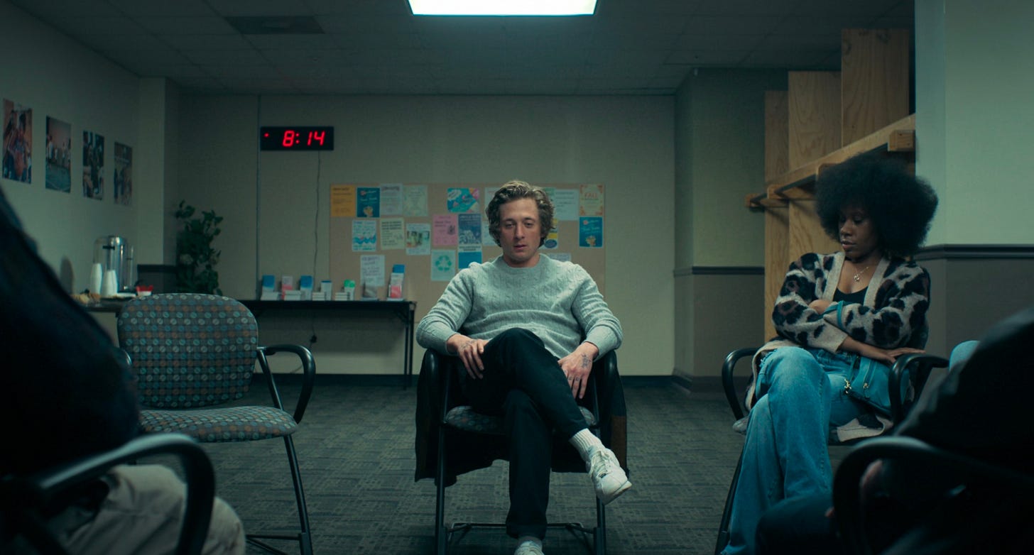 Carmy sits in an AA meeting with a large digital red clock in the background