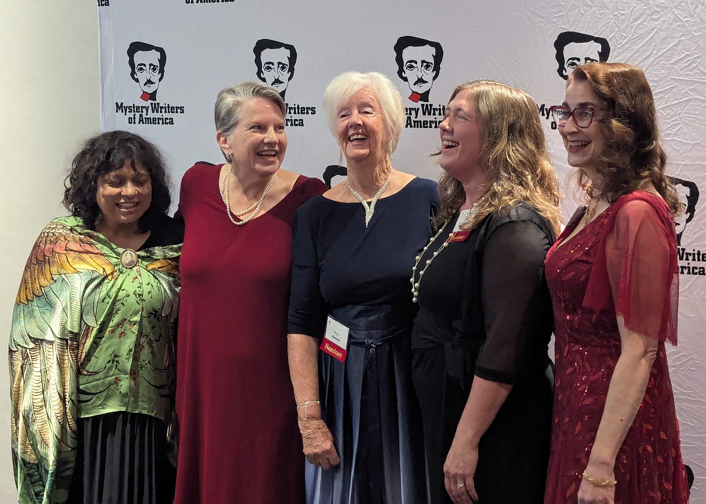 Five women standing together and laughing in front of a sign advertising the Mystery Writers of America