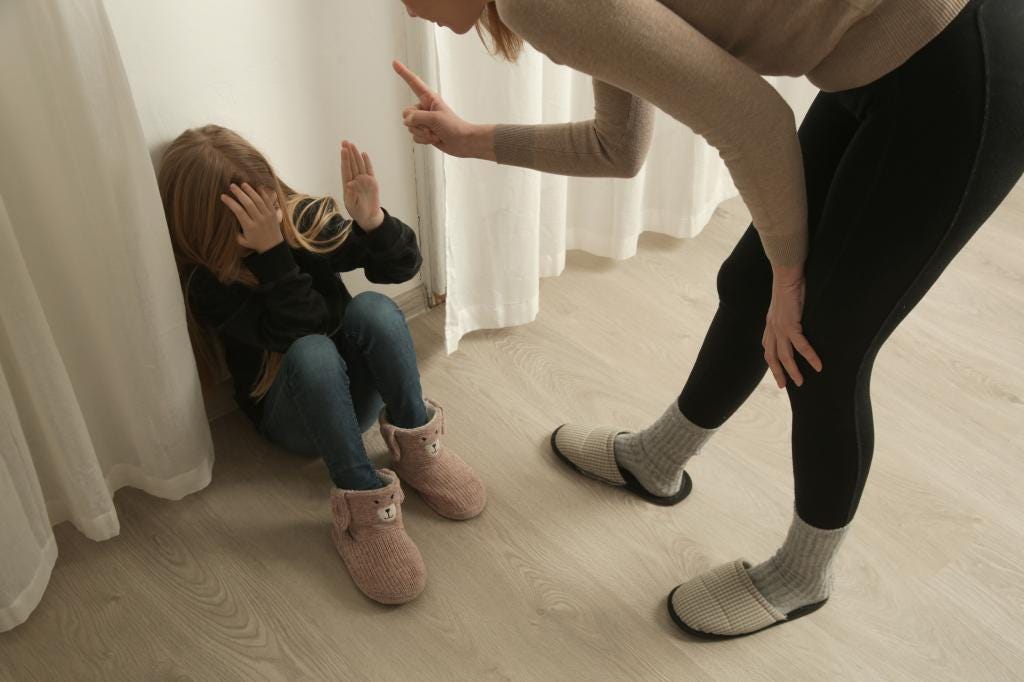 An angry mother yelling at and pointing a finger at a scared child, who is huddled in a corner covering their face. An angry mother yelling at and pointing a finger at a scared child, who is huddled in a corner covering their face.