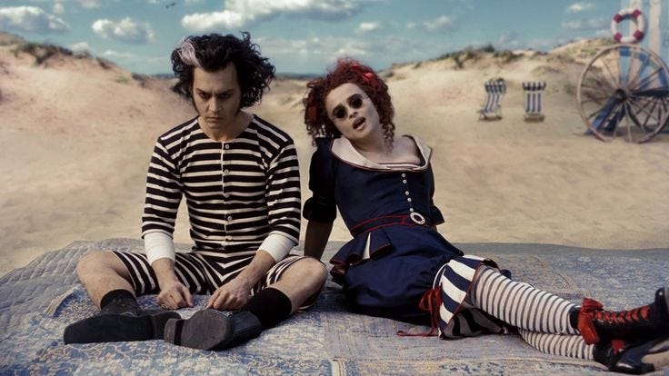 This may contain: two people are sitting on the beach with their feet in the sand and one is wearing striped socks