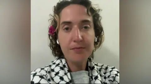 RTÉ A woman with short hair sitting looking at the camera. She is wearing a keffiyeh, has earbuds in and has a flower above her ear. RTÉ A woman with short hair sitting looking at the camera. She is wearing a keffiyeh, has earbuds in and has a flower above her ear.