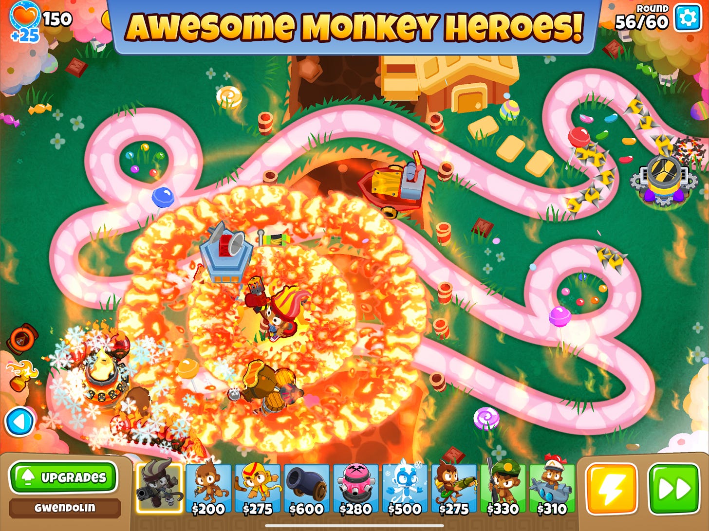 Colorful battle scene from Bloons TD 6 showing monkey towers popping balloons on a winding candy path. Colorful battle scene from Bloons TD 6 showing monkey towers popping balloons on a winding candy path.