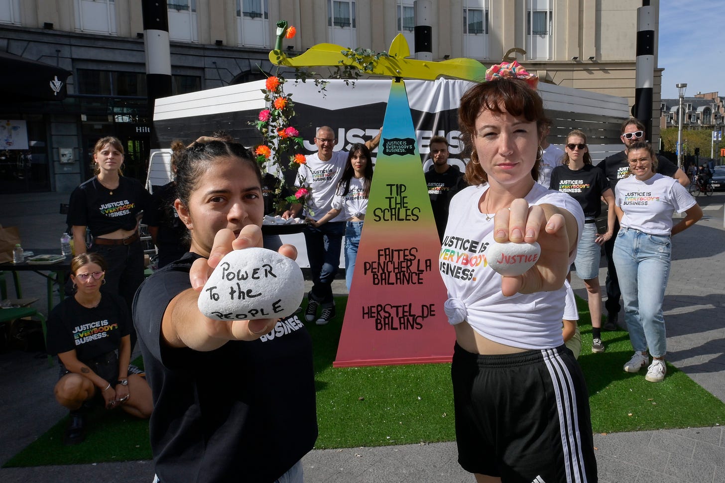 Coalition campaigners stand outside a prop of a giant scales that say 'Tip the scales' and are holding pebbles that have been marked with the words 'Power to the people' and 'Justice'