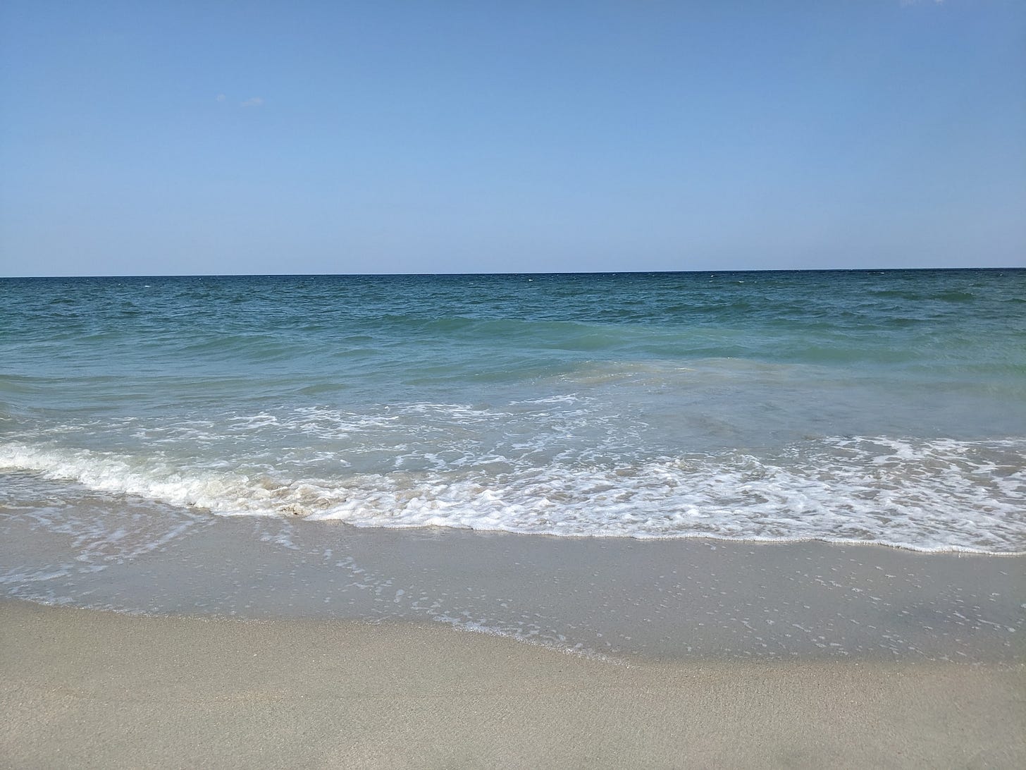 An aqua and blue ocean along the shoreline with a blue sky in the background.