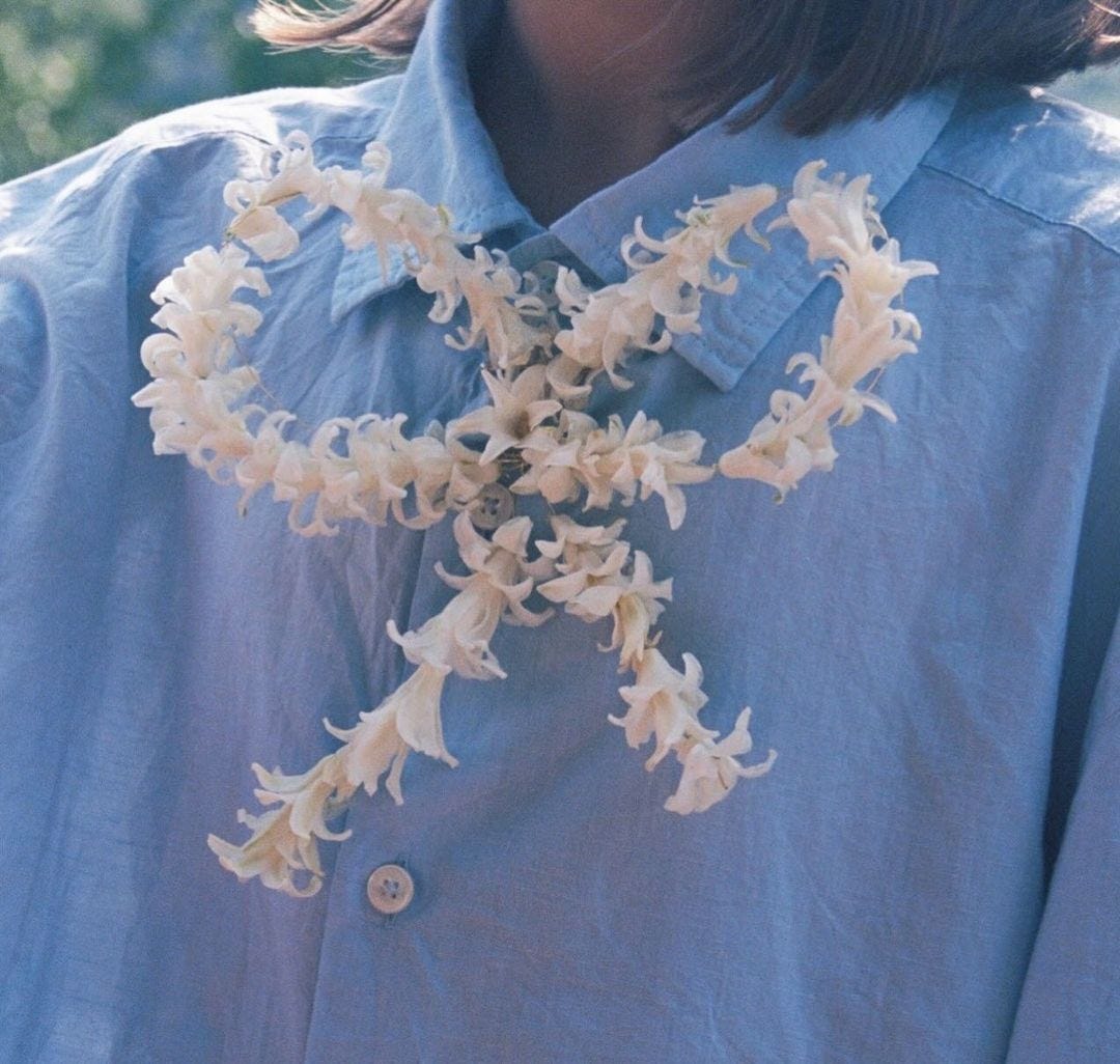 Woman wearing blue collared shirt. white flower in a bow formation