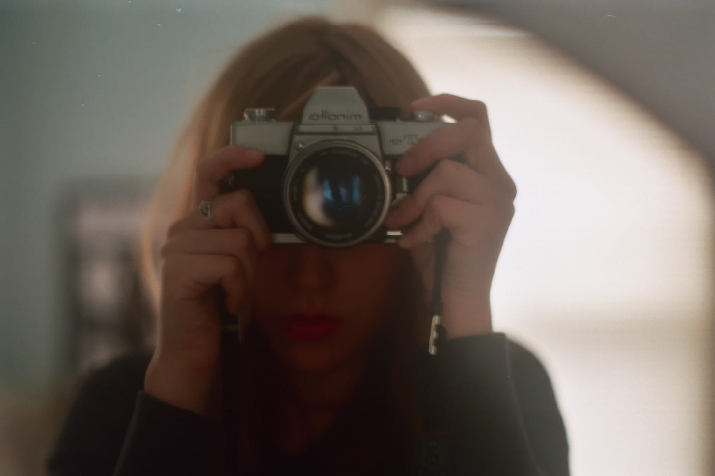 ID: Alej taking a photo of themself in a mirror with a minolta camera, their face is obscured.