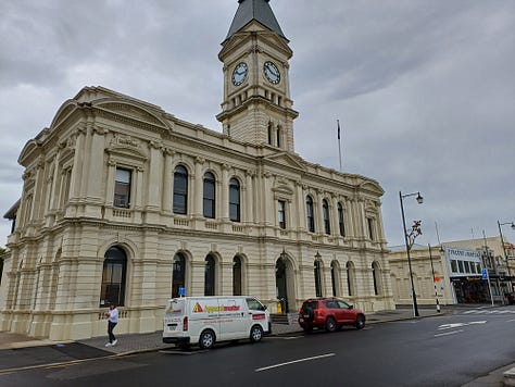 A series of stone buildings, created in a variety of styles, from fairly plain and study to huge and ornate. All of the buildings are made from or incorporate creamy limestone, some soot-blackened or weathered. On the right top is a locomotive engine cab with a large screw mounted at the front, located to indicate that it has just burst up out of the ground. The bottom right features a whitestone bridge fording a stream, over which the main street is laid.