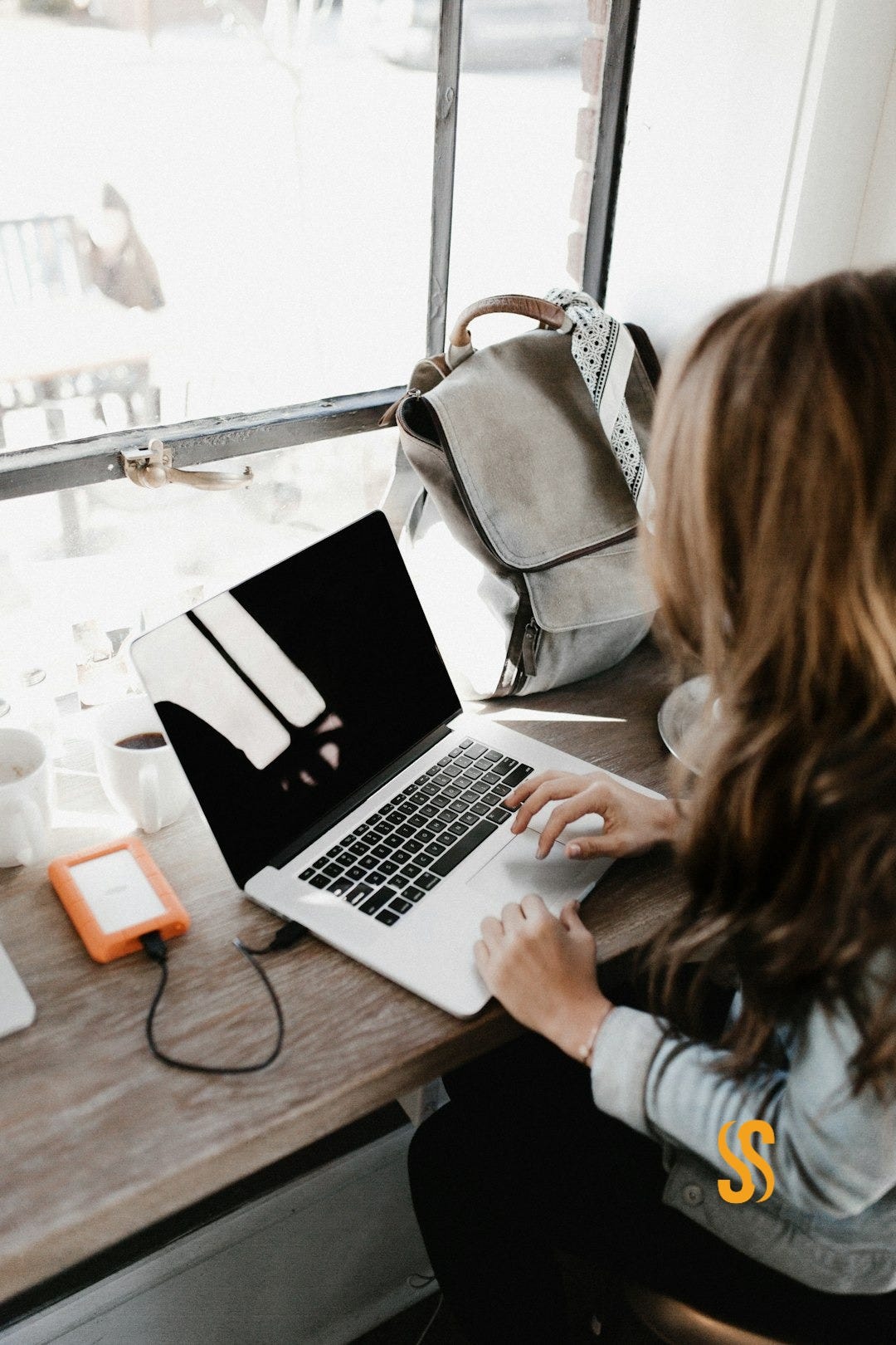 girl wearing grey long-sleeved shirt using MacBook Pro on brown wooden table girl wearing grey long-sleeved shirt using MacBook Pro on brown wooden table