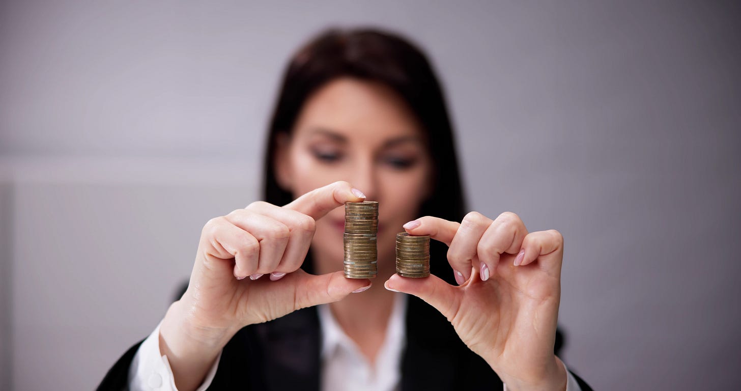Young businesswoman dressed in a suit contemplates two stacks of coins that are different heights