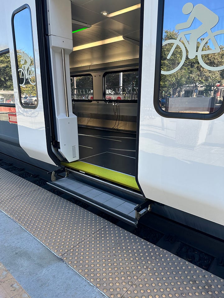Photograph showing the doors of a train. The doors are open. The emphasis is on the stairs of the train. The old train has multiple steps and a large gap between the platform and the train. The newer train shows a much smaller gap and a low floor, single step entrance of the train.
