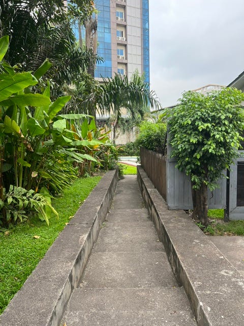 A white-washed stucco home with dark metal bars on the windows and a paved walkway leading between a house and a garden