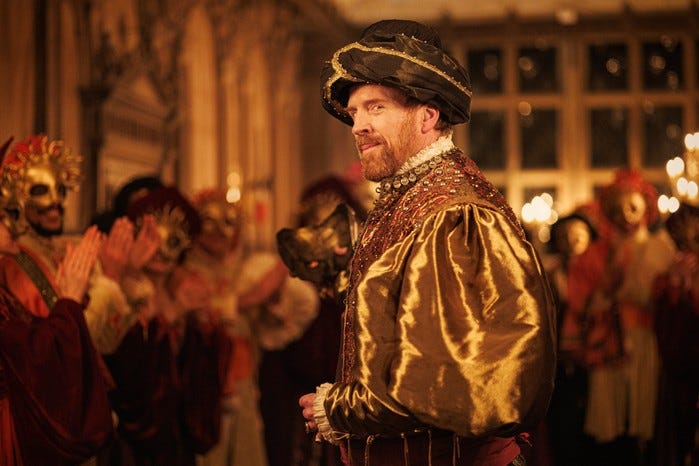 Damian Lewis as King Henry VIII standing in a hall full of people and turning round to look at something in Wolf Hall: The Mirror and the Light.