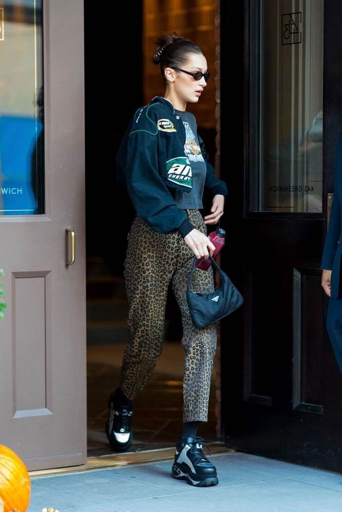 This may contain: a woman in black jacket and leopard print pants walking out of a building with her handbag