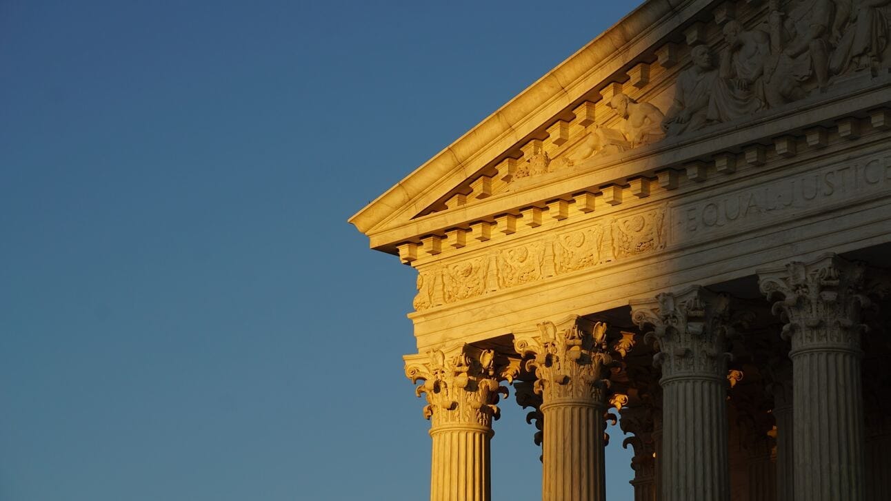 On the right side of the image, the Supreme Court Building sits half in shadow, half in dusky sunlight against a blue sky.