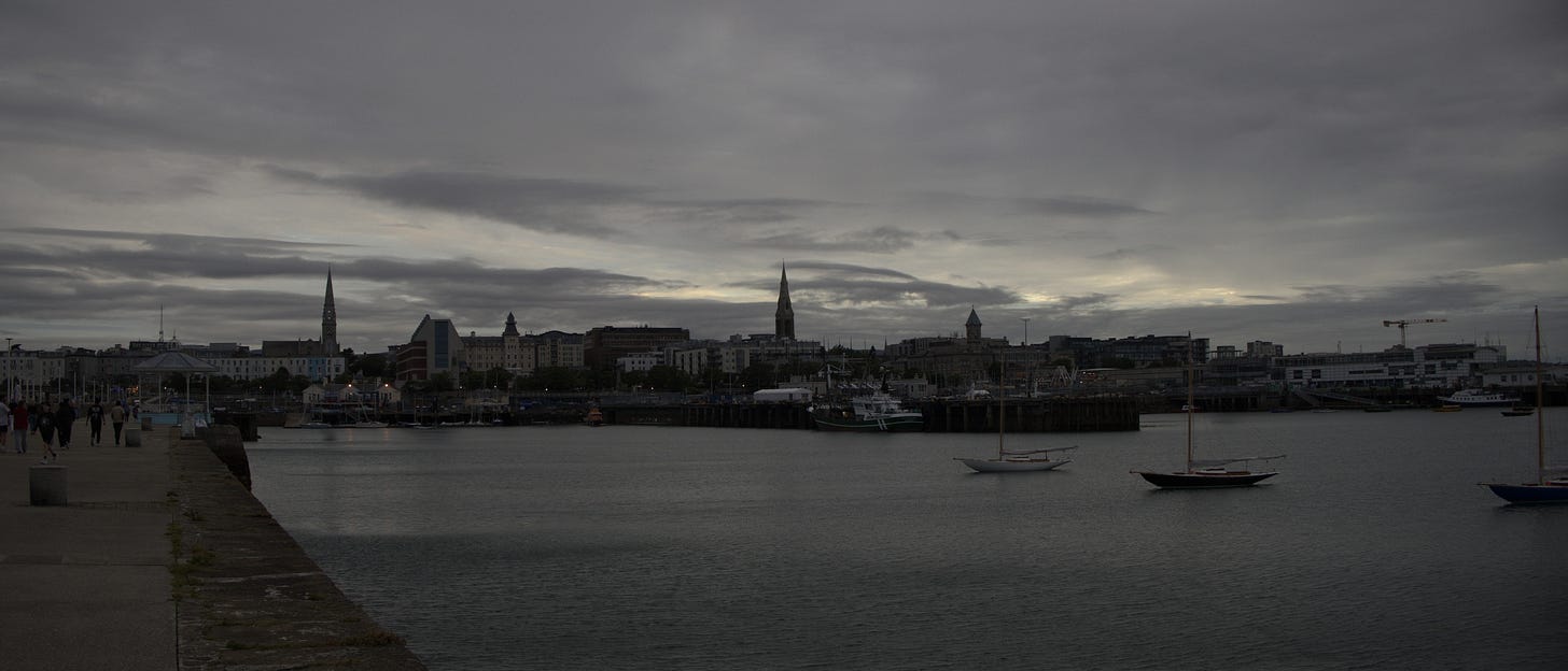 The same Dún Laoghaire harbour scene in flat, cool grey tones, overcast sky, and muted water, showing the unedited version of the previous photo.