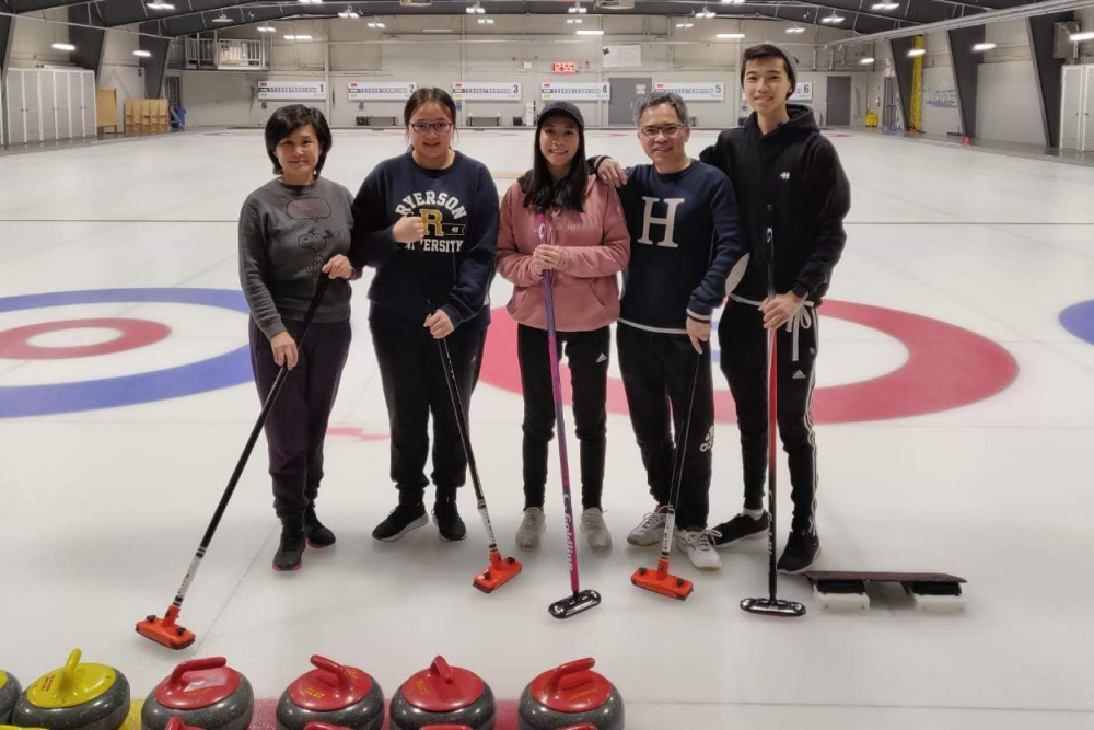 5 people standing on a curling rink smiling and posing. 5 people standing on a curling rink smiling and posing.