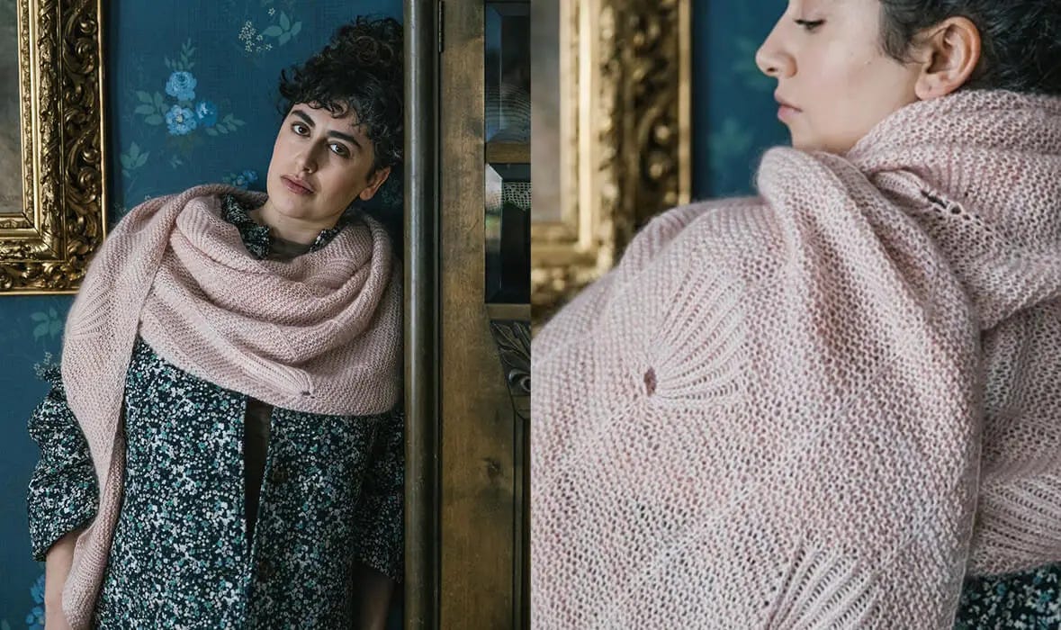  A woman leans against a wardrobe, wearing a pink hand-knit shawl and a blue and white dotted coat.