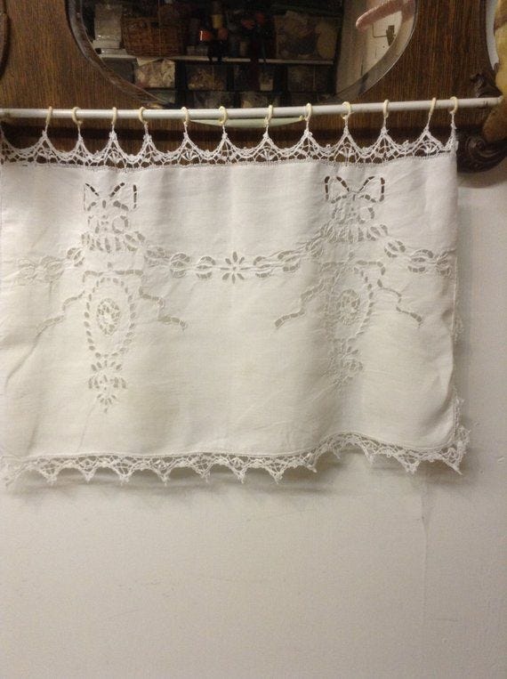This may contain: a white curtain hanging on the side of a wall next to a wooden shelf and mirror