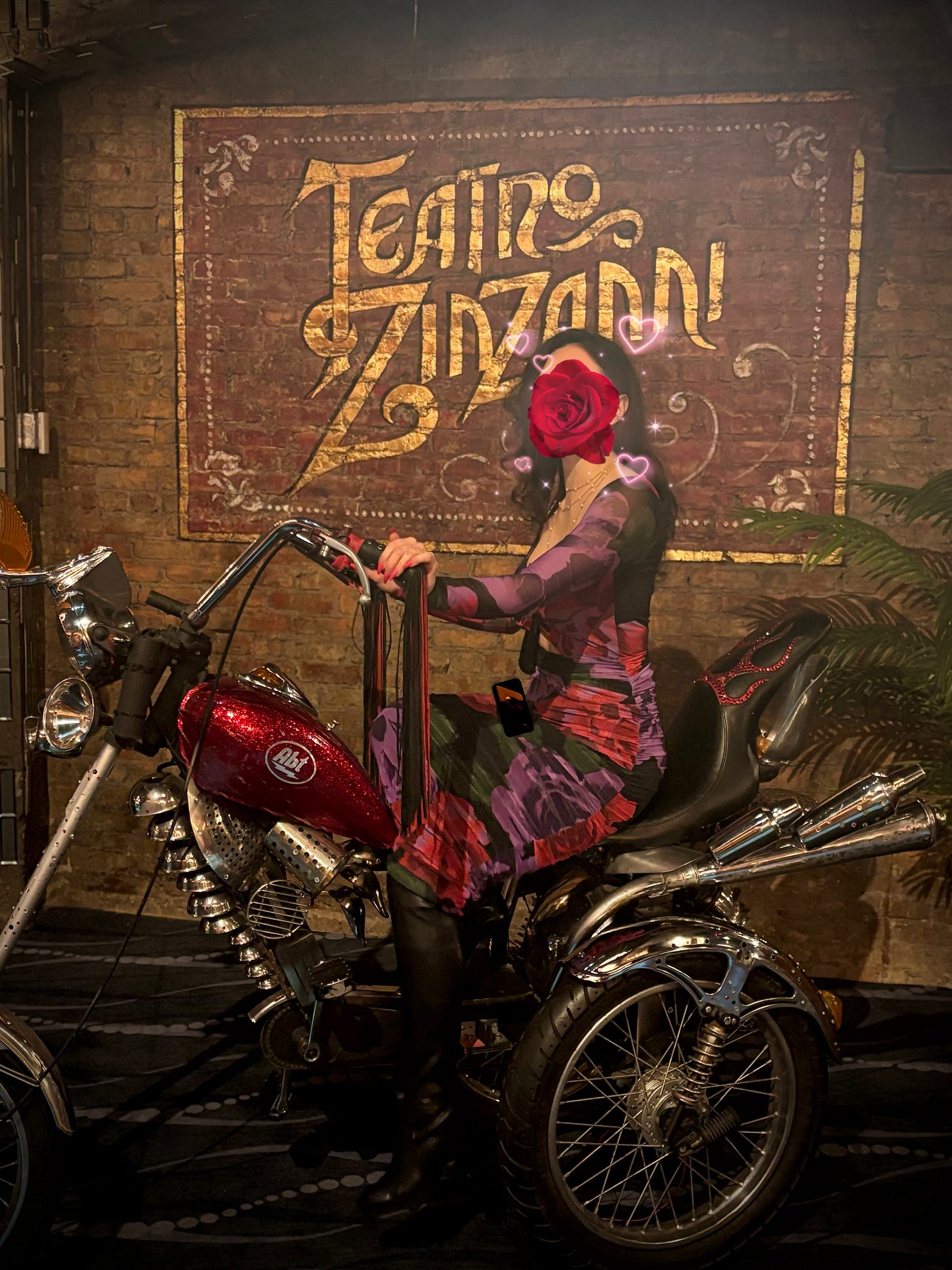 Chicago provider Elena Marchetti on a motorbike in a form-fitting, mid-length red and purple flowered dress in the lobby of a theater