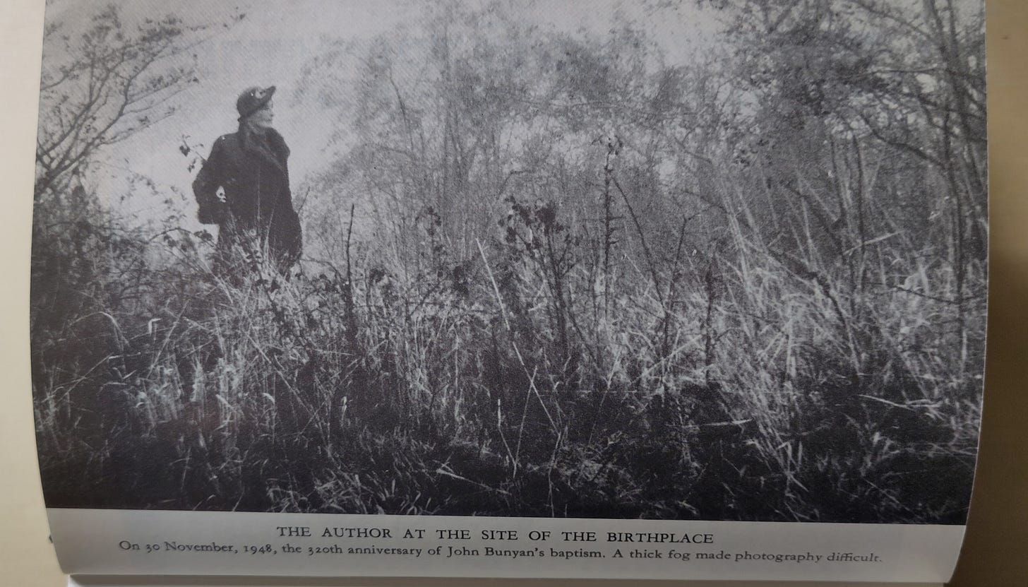 Black and white photo of a woman in a hat and coat in a foggy landscape.