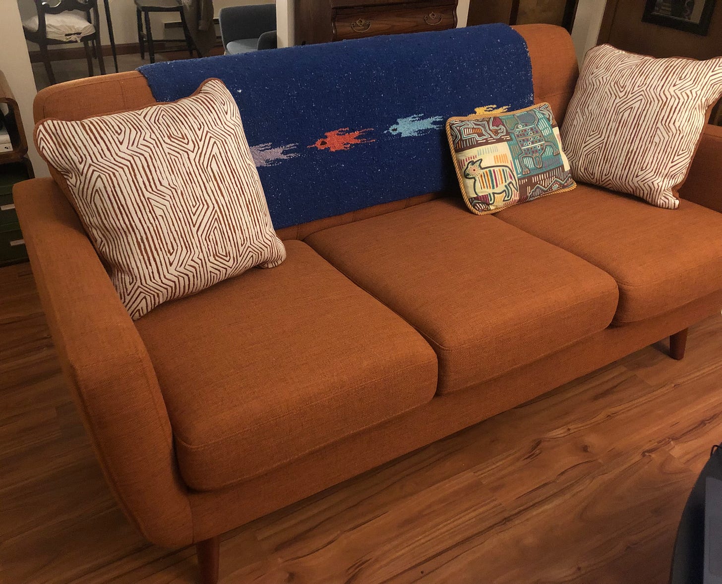 A dark orange couch with a dark blue blanket over the back and patterned throw pillows.