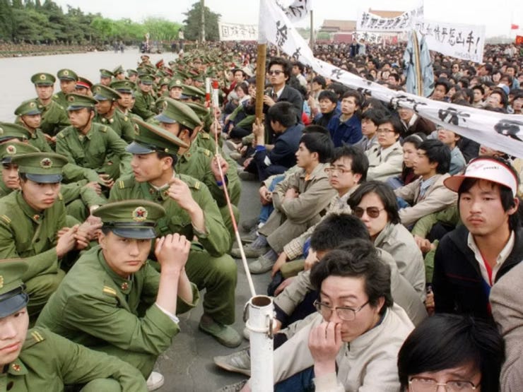 Unarmed soldiers sitting and squatting beside peaceful students, separated only by a thin barrier.