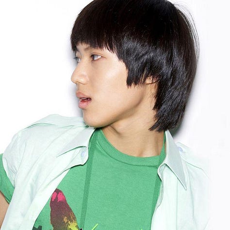 Taemin stands in casual late-2000s streetwear, wearing a layered graphic T-shirt, skinny jeans, and sneakers. His hair is cut in the rounded style associated with SHINee's debut era. 