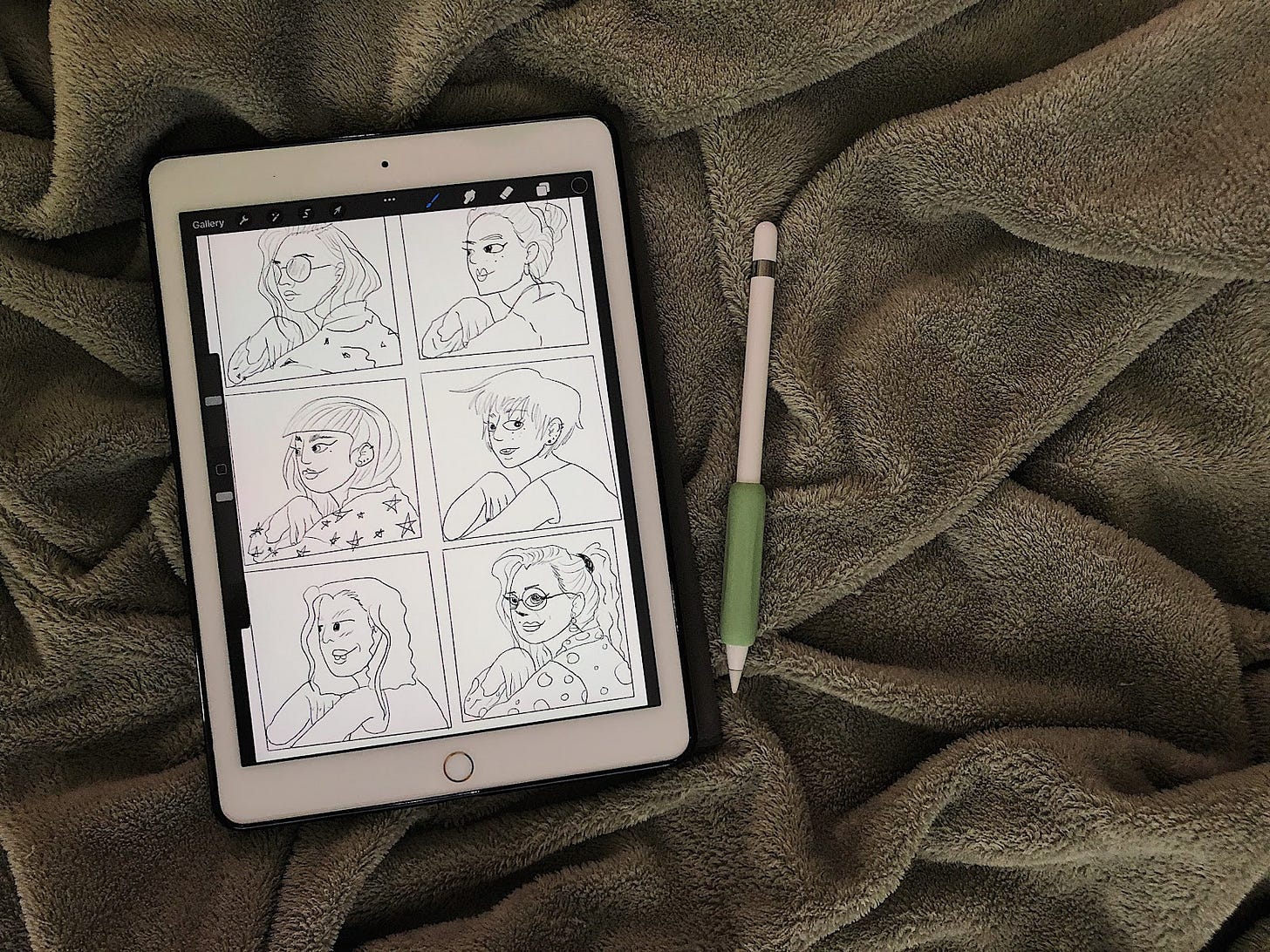 An overhead view of an ipad with six women drawn on it with an apple pencil next to it on a green blanket