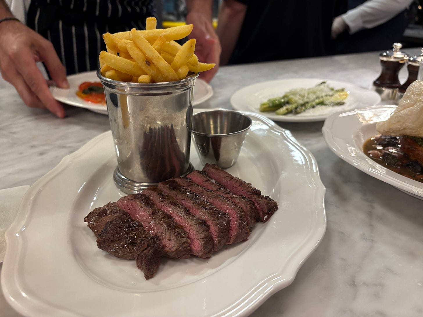 Thinly sliced medium rare steak shares a plate with a cup of fries and a small pot of sauce Thinly sliced medium rare steak shares a plate with a cup of fries and a small pot of sauce