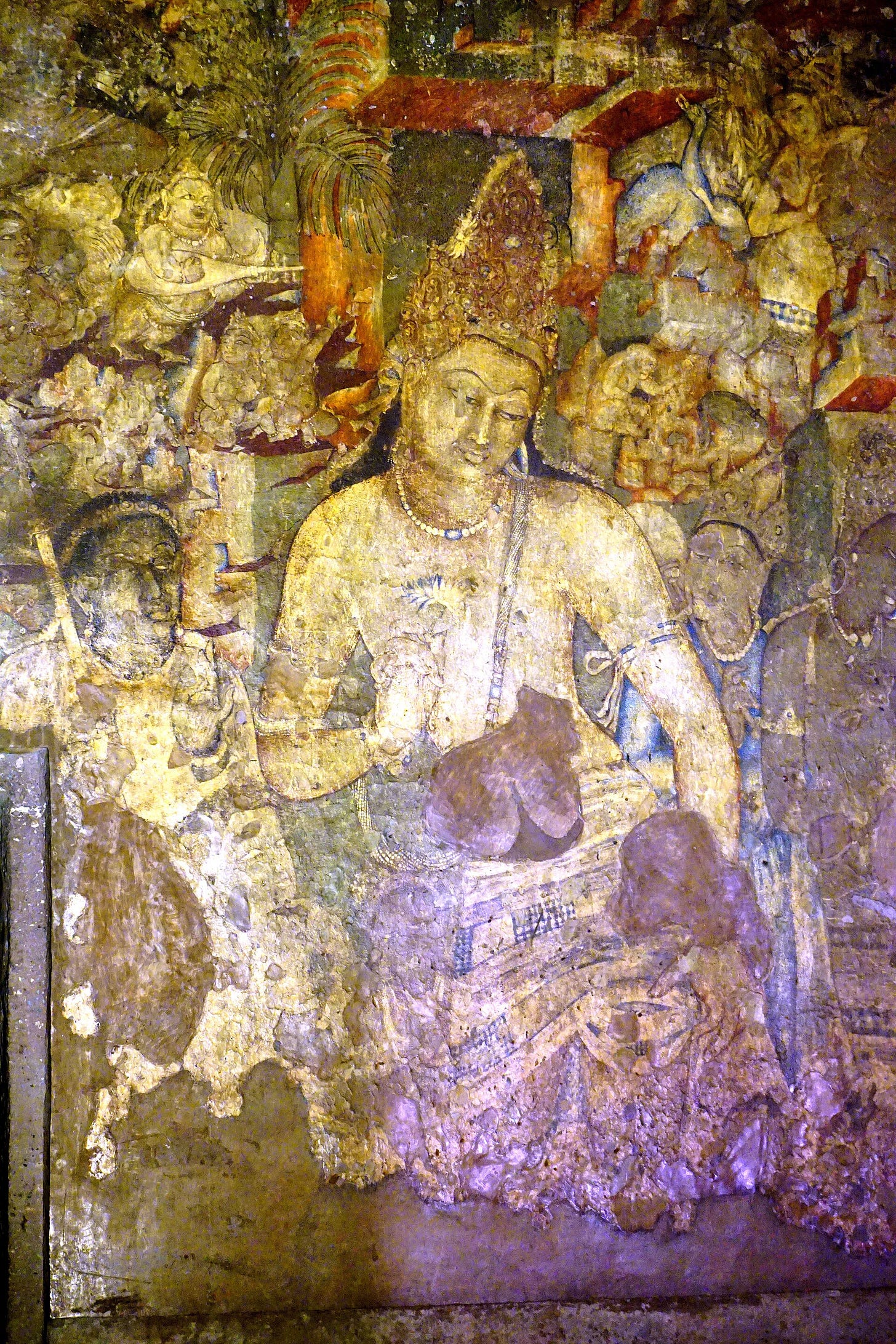 An ancient wall painting of a crowned Buddhist figure with lowered eyes and a tilted head, holding a blue lotus, in the dim light of a cave. An ancient wall painting of a crowned Buddhist figure with lowered eyes and a tilted head, holding a blue lotus, in the dim light of a cave.