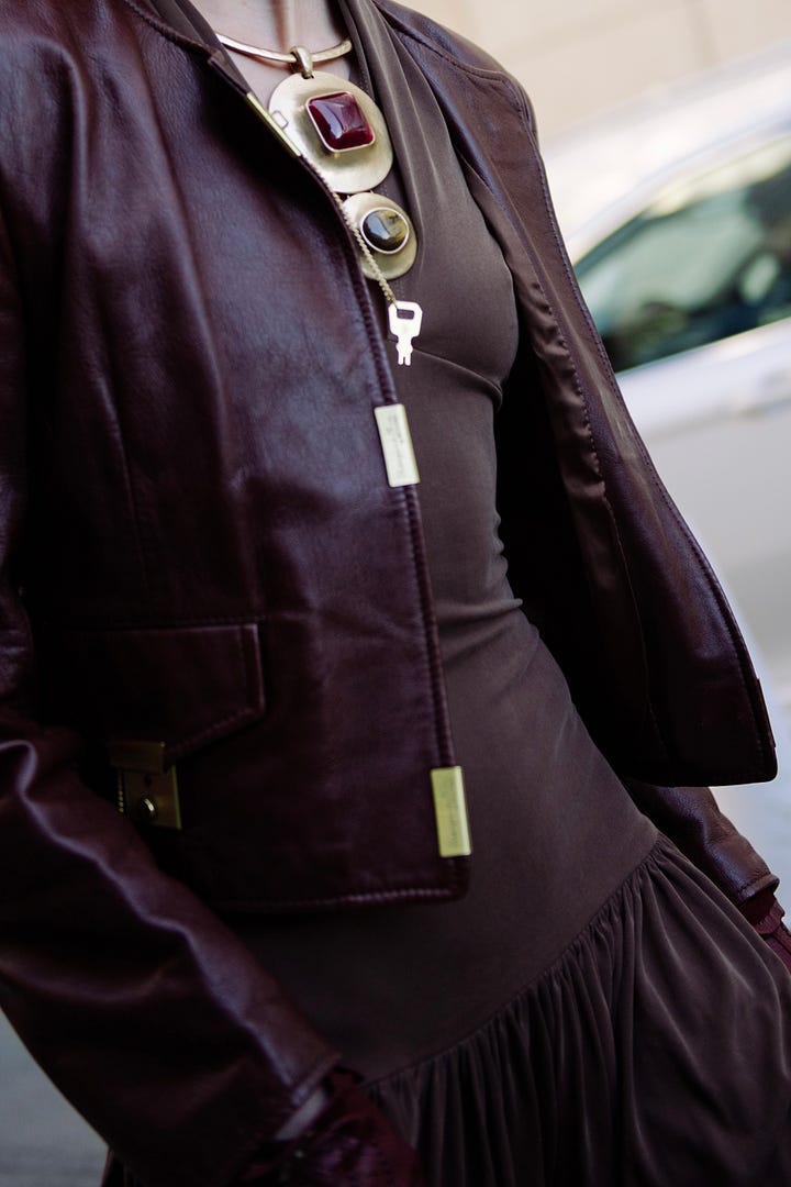 Street style image of a fashionable woman in olive outerwear during NYFW; close-up of a burgundy vintage leather jacket styled for fashion week.